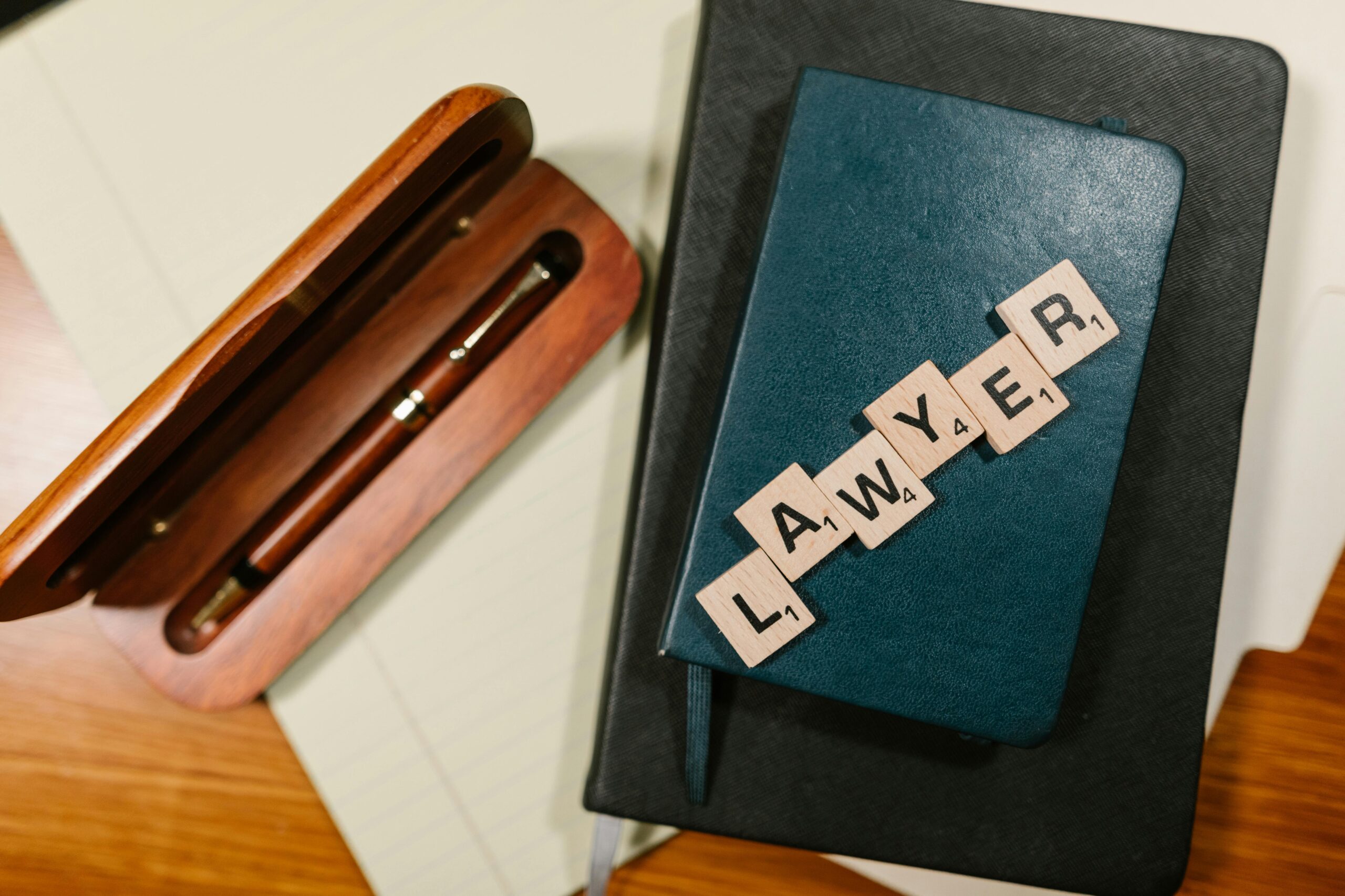 Scrabble tiles spelling 'LAWYER' on a blue notebook with a wooden pen case, overhead view.